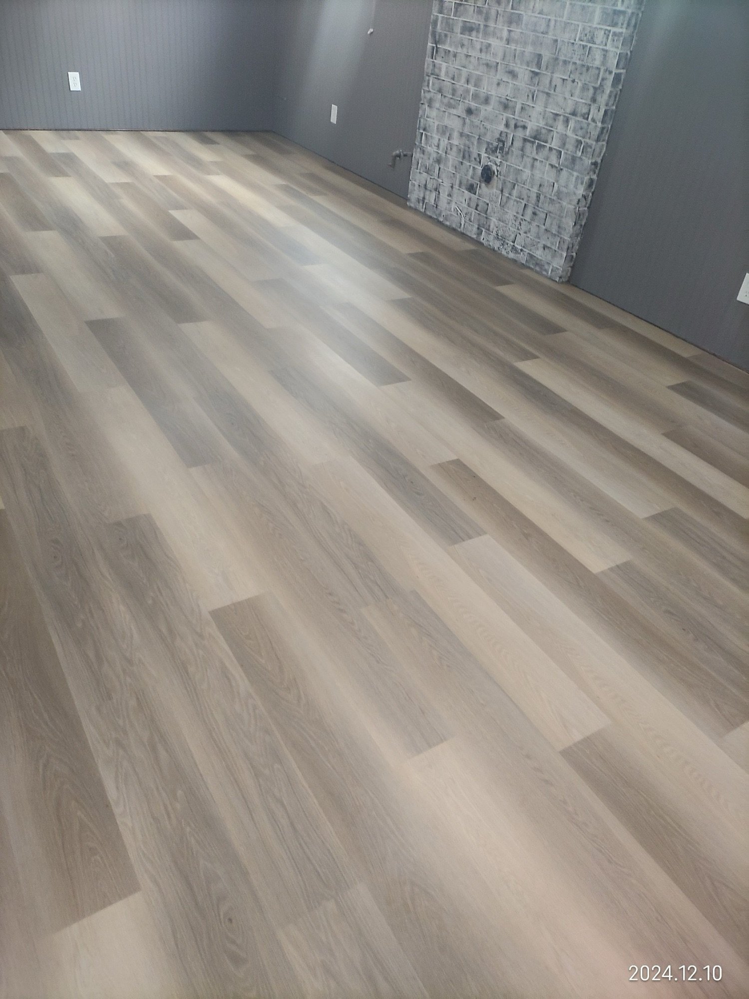 Freshly installed luxury vinyl plank flooring in an empty room with a brick chimney