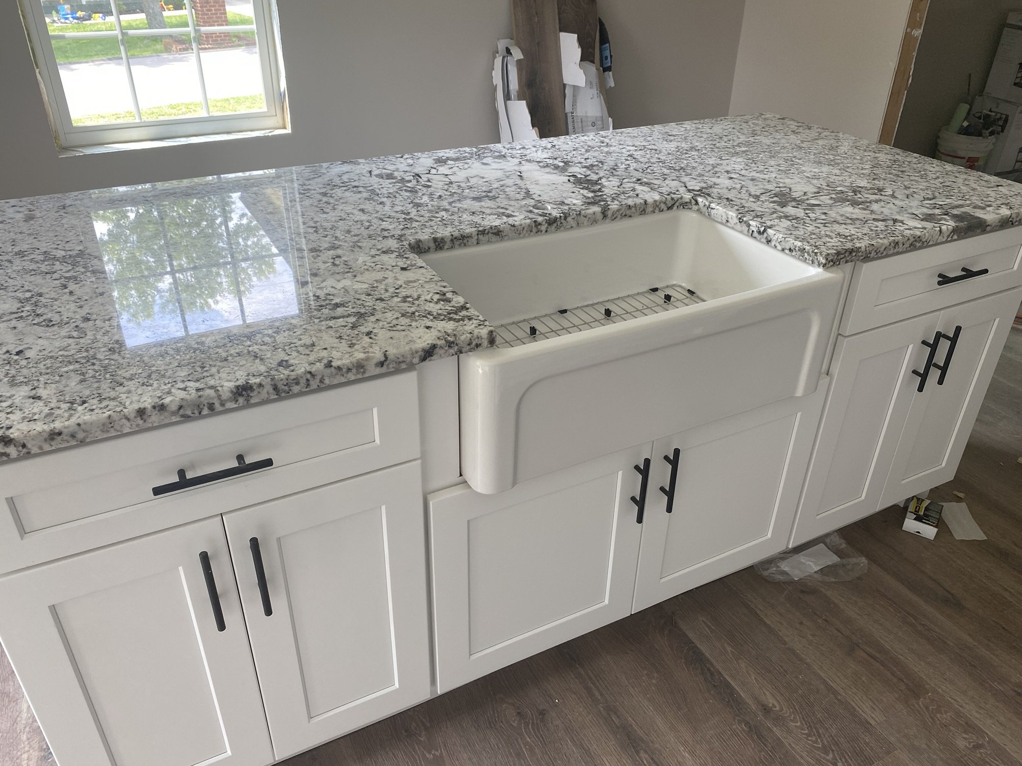 White shaker island with a fireclay farmhouse sink and white and gray granite countertop