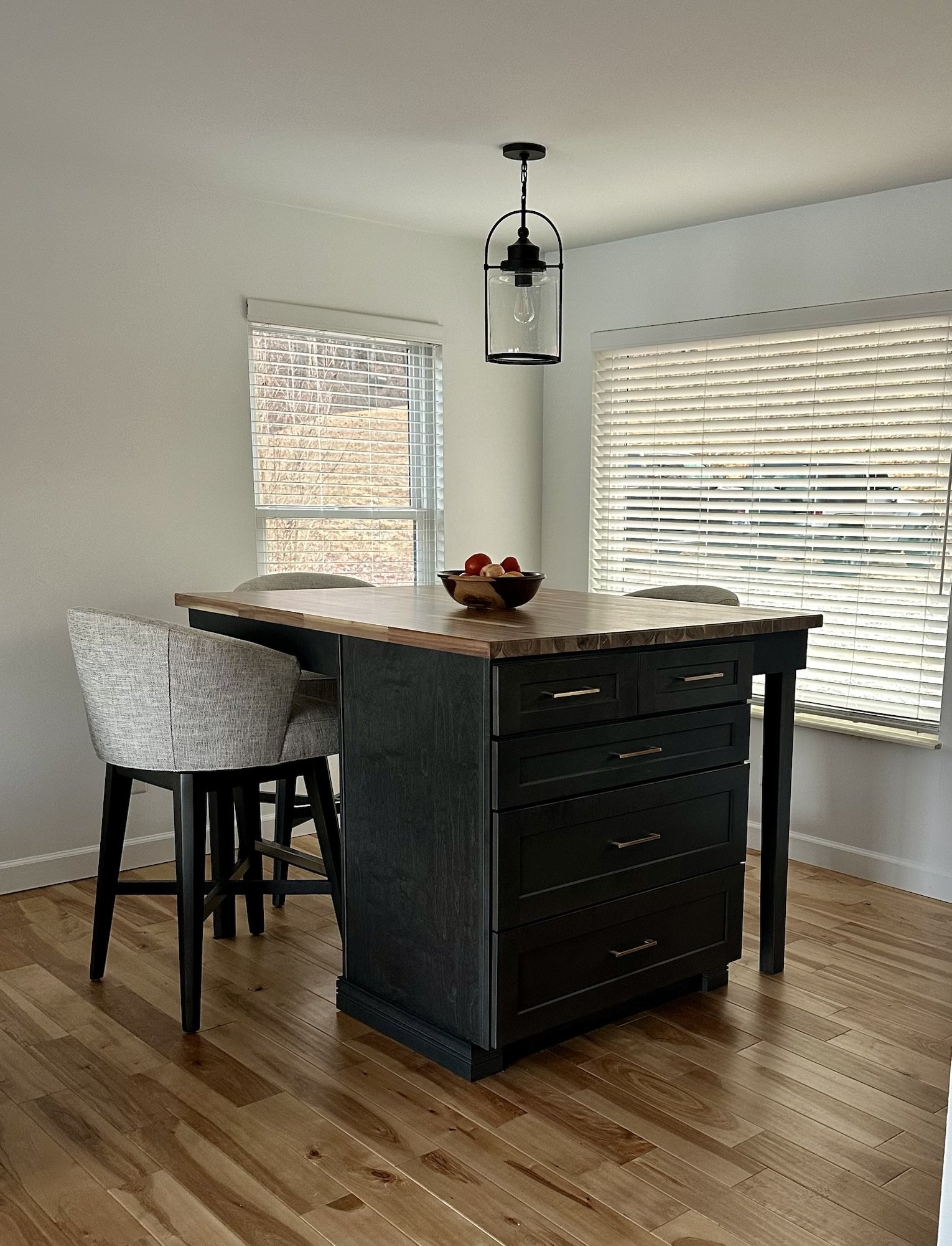 Black kitchen island with a butcher block top and upholstered stools on hickory flooring