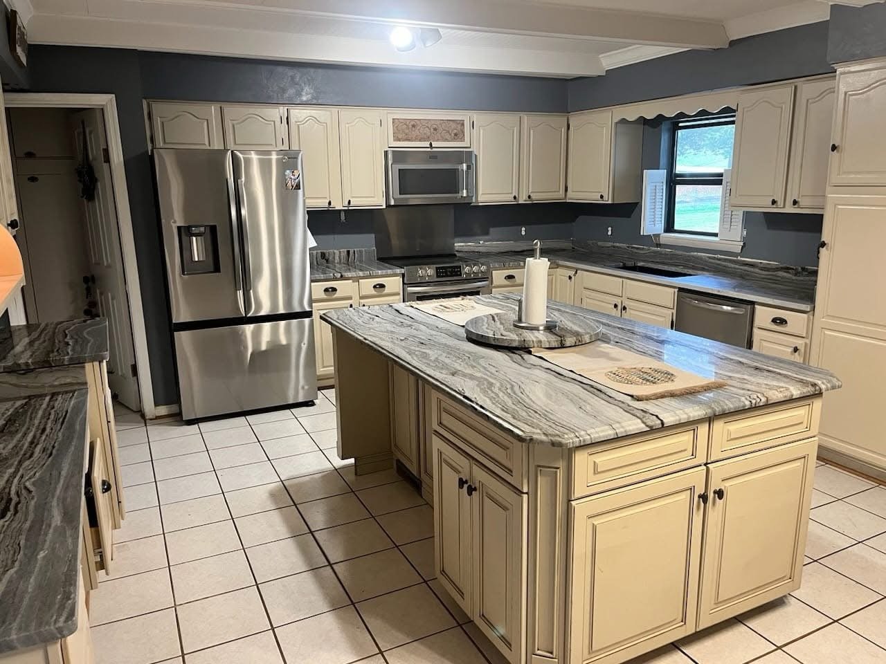 Cream kitchen cabinets with fantasy brown marble countertops and a large island