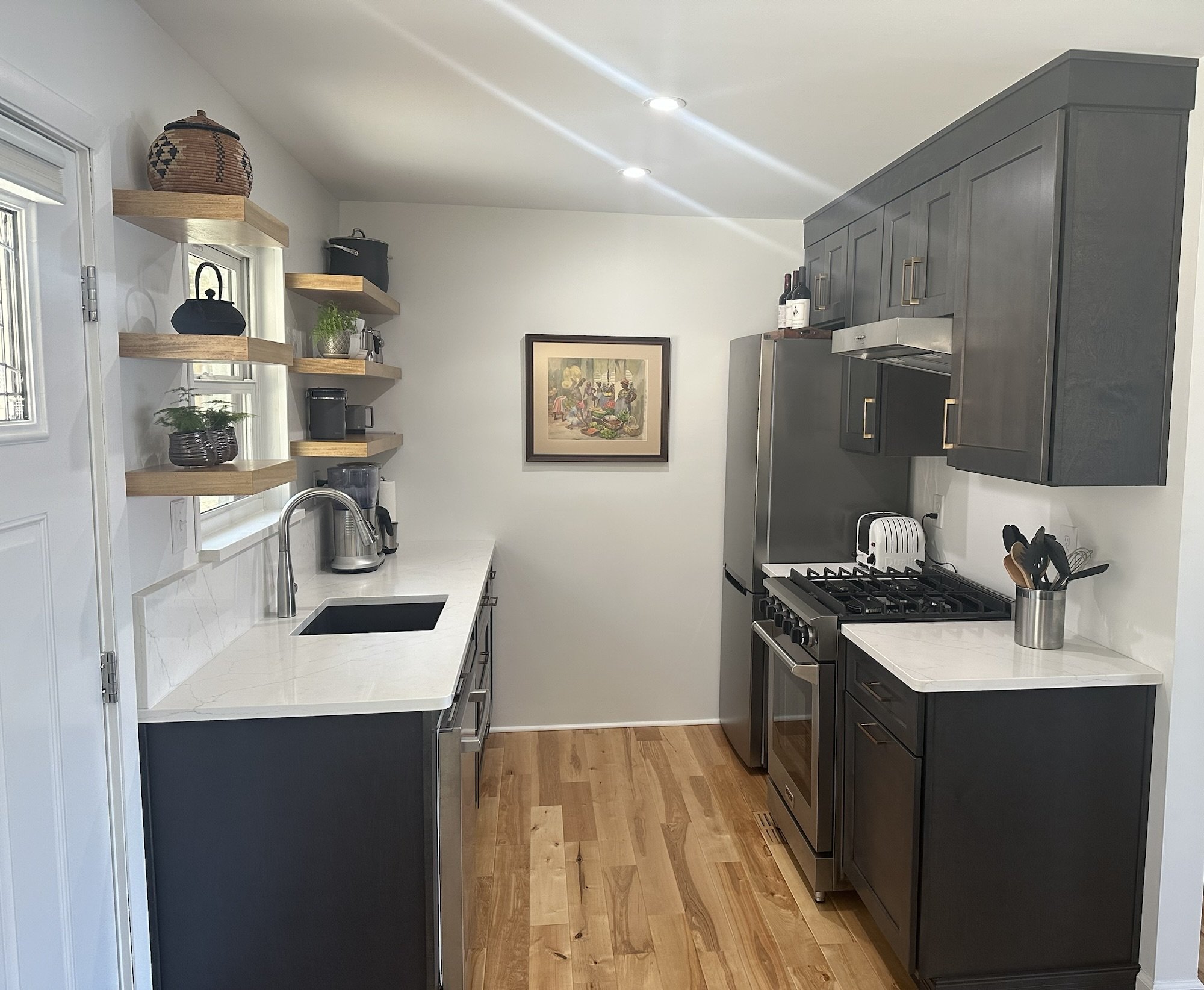 Charcoal gray galley kitchen with white marble look quartz counters and hickory hardwood flooring