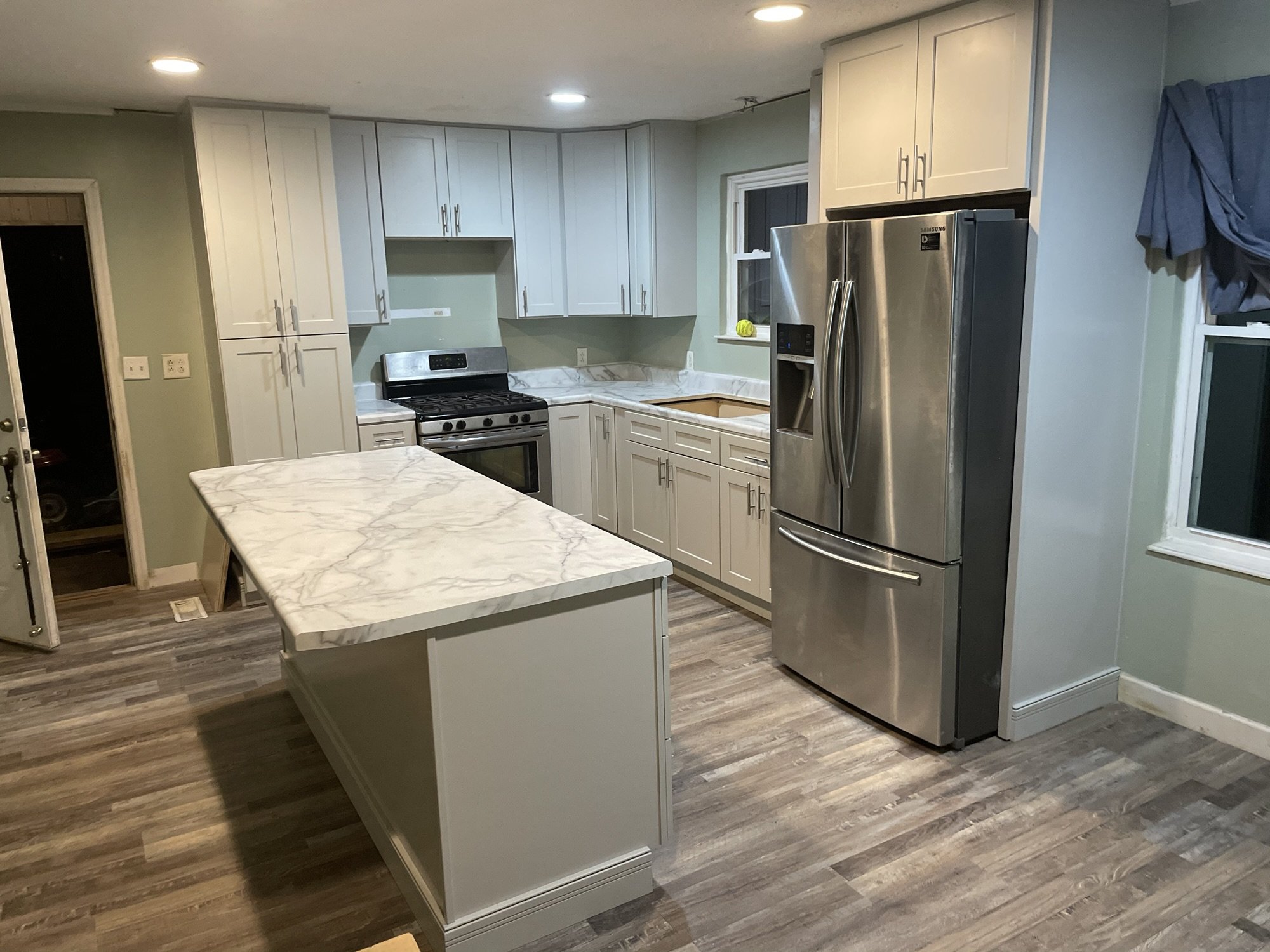 Greige shaker kitchen cabinets with a marble look island and gray plank flooring