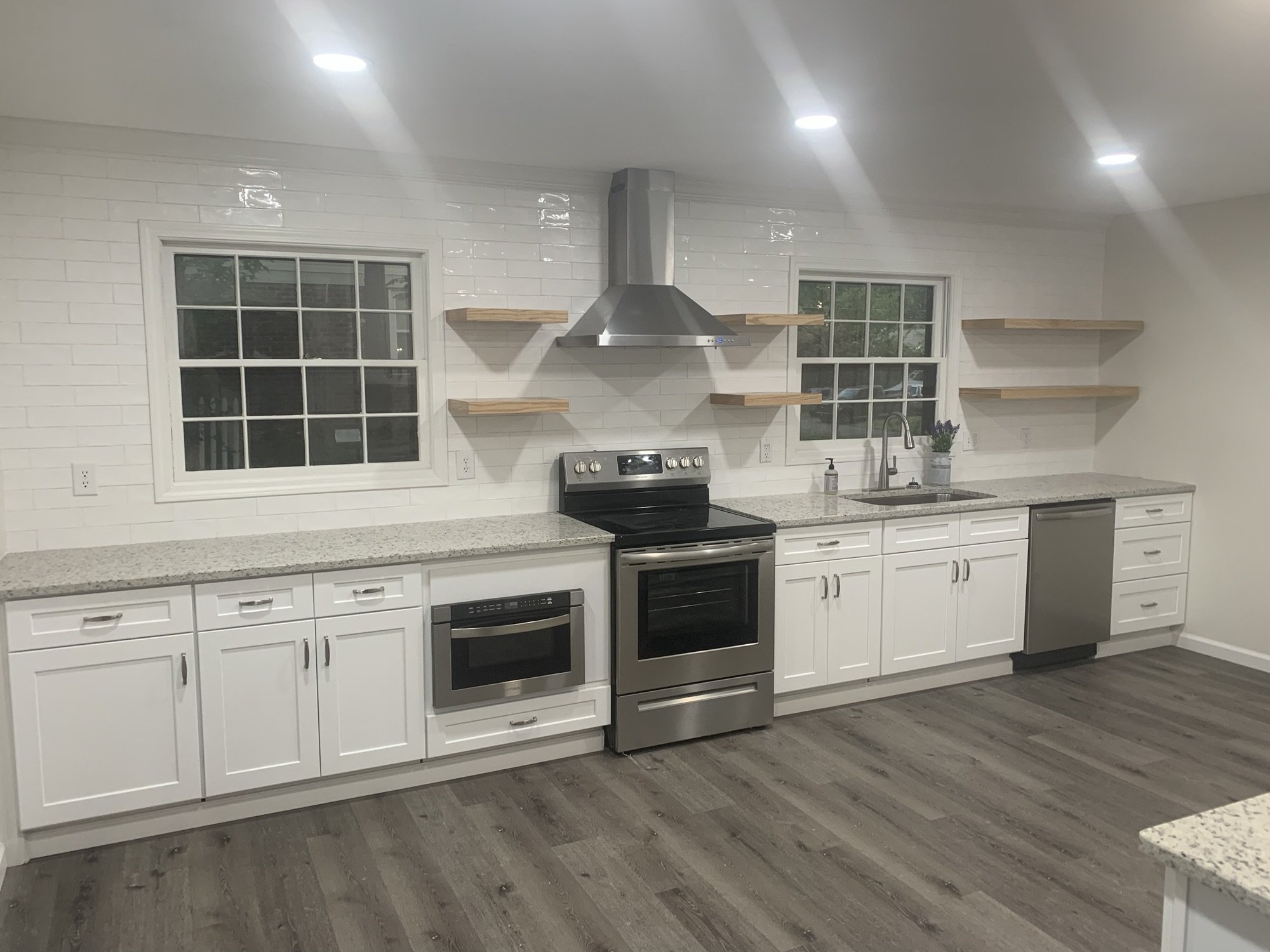White shaker kitchen with full wall subway tile, speckled granite counters, and oak floating shelves