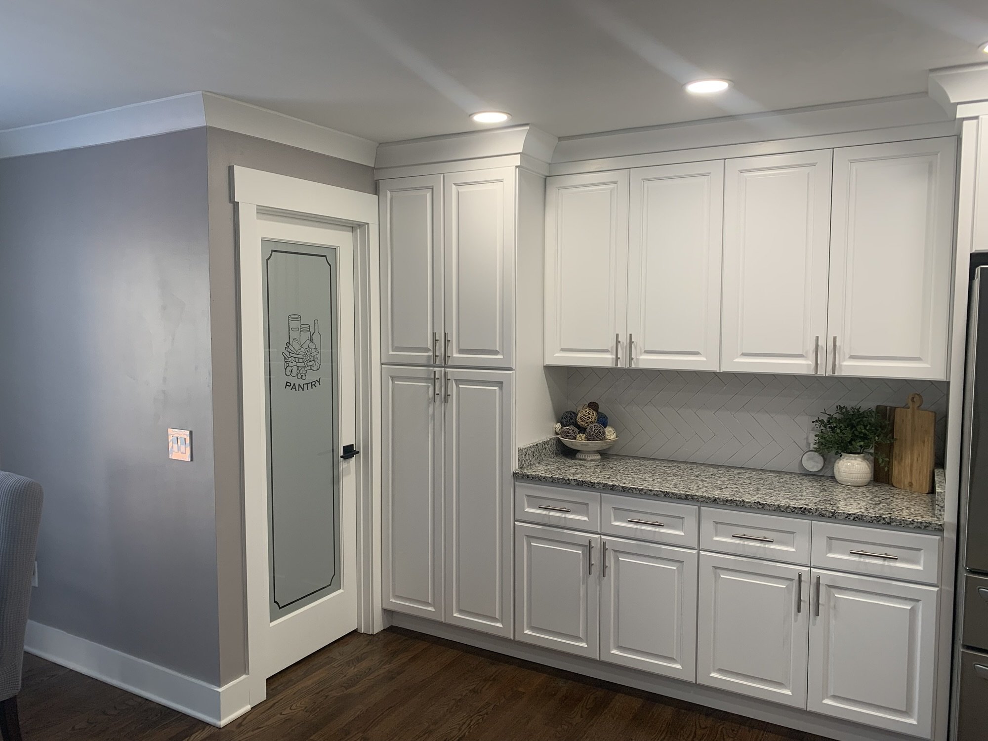 White kitchen cabinets with granite counter, herringbone tile backsplash, and pantry door